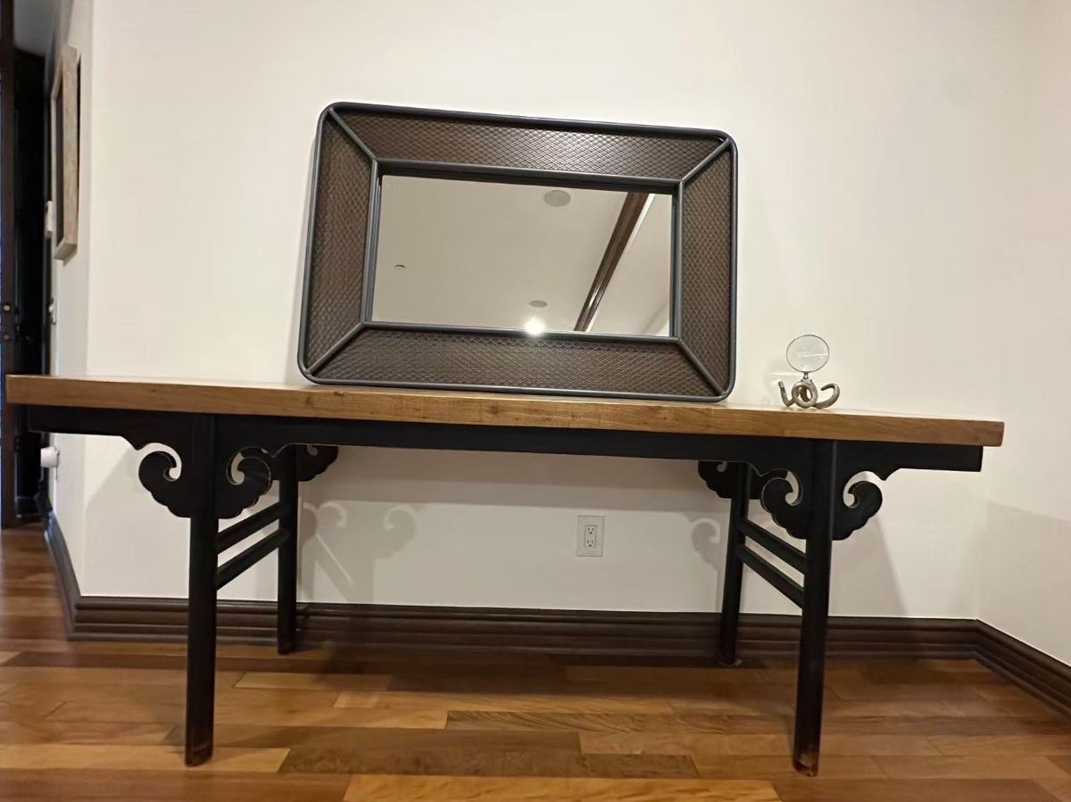 Elegant console table with a natural wood grain top and a black painted base. This piece has decorative scrolled spandrels and horizontal stretchers between the legs. The table is constructed from wood and features a long, narrow profile.