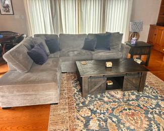 Plush grey velvet sectional sofa with a left-facing chaise. This L-shaped couch has soft fabric upholstery and includes matching dark blue throw pillows.