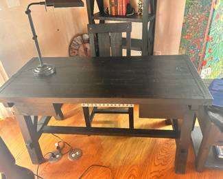Solid wood desk with a dark espresso finish. This piece has a rustic plank-style top and a sturdy trestle base with a crossbar support. The design includes two small drawers on the front and decorative metal stud detailing along the underside of the desktop.