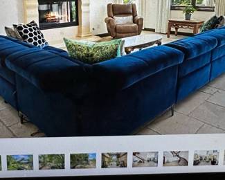 Reclining Luxurious L-shaped sectional sofa is upholstered in navy blue velvet. This large seating arrangement has a tufted, channel-stitched design on the backrest and seat cushions. The piece is supported by slim, dark metal legs and consists of multiple modular components joined together.