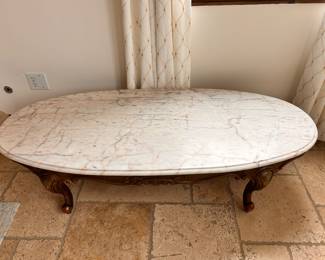 Elegant coffee table has a white marble top with pink and grey veining. The base is carved wood with a dark finish and cabriole legs. This piece features ornate scrollwork along the apron and legs.