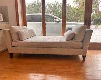 Upholstered light gray daybed has a symmetrical design with flared arms on both ends. This piece includes two large back cushions and two smaller bolster pillows. The frame is supported by dark wood tapered legs. There are visible stains on the front base and seat cushion.  Estimated (WxDxH): 80 x 34 x 32 in