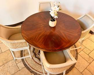 Sturdy wood dining set includes a round pedestal table and four matching chairs. The tabletop has a sunburst wood veneer pattern in a dark brown finish. Each chair has a woven rattan-style exterior, light-colored upholstery, and nailhead trim along the backrest. The table is supported by a heavy, carved pedestal base. Belonged to a celebrity before and need pickup arrangement.