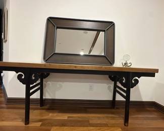 Elegant console table with a natural wood grain top and a black painted base. This piece has decorative scrolled spandrels and horizontal stretchers between the legs. The table is constructed from wood and features a long, narrow profile.
