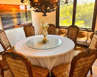 Elegant dining set includes a large round wooden table covered with a white tablecloth and a glass lazy susan. Eight high-back chairs have carved wood frames and gold-toned damask upholstery. The wood has a warm brown finish. For table $560 For Eight high-back chair $50/each For Twelve Blue velvet tufted dining chair with nailhead trim and dark wood legs, $50/each For Six Modern Tan Faux Leather Dining Chairs with Black Metal Sled Legs, $45/each
