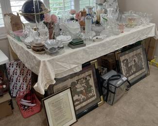 This table features several different glass and crystal serving dishes, including a playful straw dispenser, a polished globe, two framed Egyptian-inspired artworks, and more.  Come see the selection for a better look.