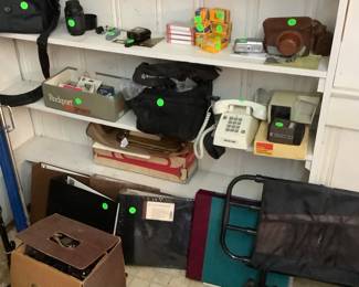 A shelf full of different cameras, cases. Mi’m sure some were used to take pictures from their travels and pictures of things they painted.