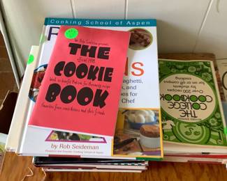 Along with other books, there are several cook books sitting in a small solid oak table.