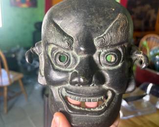  A remarkable pair of antique iron masks, believed to be 19th century, brought to the United States by a diplomat with extensive ties to East Asia. One is a fully three-dimensional demon/oni face with jade-green glass eyes and detailed etched features. The second is a flat iron mask with a fierce expression, jade-green glass eyes, and Chinese characters inscribed on the reverse, with a wire hanger. Both show beautiful age patina. Exceptional collector's pieces with genuine provenance.