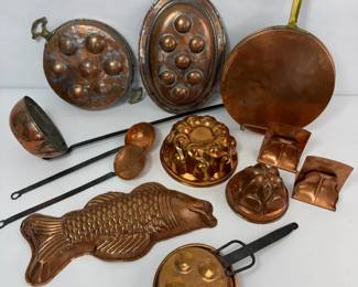 Assorted copper cookware and molds including pans, ladles, and decorative forms with classic patina.