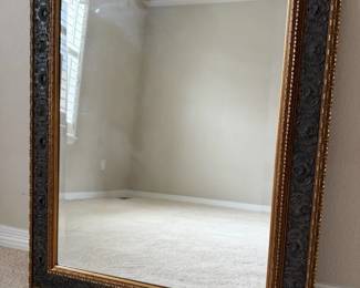Striking wall mirror featuring an ornate giltstyle frame with rich gold tones and distressed