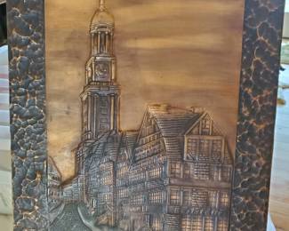 This item is a copper relief wall sculpture. Vintage Hammered Copper 16X26. The artwork depicts a European street scene, specifically featuring the St. Michaelis Church (St. Michael's Church) in Hamburg, Germany, often referred to as "Der Michel."