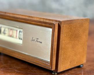 Seth Thomas vintage wooden flip clock featuring a natural woodgrain exterior with a silver-tone faceplate. Displays time using a rotating flip mechanism. Includes an attached electric cord for operation. Minimal signs of wear are visible consistent with age. Tested and in working condition.