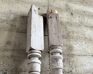 Distressed wooden architectural columns, featuring turned designs and a weathered finish indicative of their age. Each column has a square base transitioning to a detailed, rounded profile. Each measures, 96” H x 4.5” W x 4.5” D.