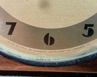 Hammond Instrument Company electric clock, made in the USA, featuring a chrome and black casing with a tan clock face and black numerals. The item includes original wiring and a two-prong plug. The back carries instructions for use and patent information. Tested and in working condition.