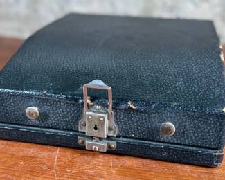 Remington Portable Typewriter featuring a black finish with orange and white round keys. Housed in its original black carrying case with a latch closure. The item shows signs of wear consistent with age and use, including minor scuffs and dust accumulation. Red label detailing model specifications is intact. Includes functioning components but may require overall maintenance or cleaning.