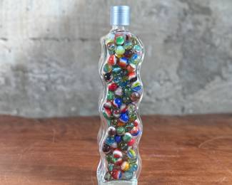 Wavy glass bottle containing a collection of colorful glass marbles. The bottle features a unique wavy design, sealed with a metallic screw cap and says “Roses”. Contents include various multicolored marbles in assorted patterns and designs. Condition appears good with no visible defects to the bottle or marbles.