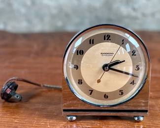 Hammond Instrument Company electric clock, made in the USA, featuring a chrome and black casing with a tan clock face and black numerals. The item includes original wiring and a two-prong plug. The back carries instructions for use and patent information. Tested and in working condition.