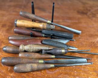 Vintage woodworking tools, including chisels and gouges with wooden handles. Some tools are marked “Buck Bros, ” known for quality craftsmanship. Handles exhibit wear consistent with age and use. The lot includes a variety of sizes and types for woodworking projects or collection purposes. Condition varies, with some minor rust and patina on metal components.