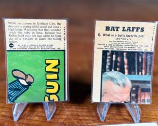 Vintage Batman trading cards, featuring original artwork and comic illustrations. Cards include storylines and engaging captions on the reverse side. Produced by National Periodical Publications, Inc., circa 1960s. Cards are displayed on stands; conditions appear fair with signs of handling and age.