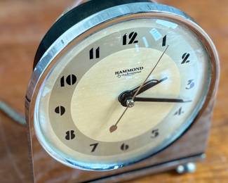 Hammond Instrument Company electric clock, made in the USA, featuring a chrome and black casing with a tan clock face and black numerals. The item includes original wiring and a two-prong plug. The back carries instructions for use and patent information. Tested and in working condition.