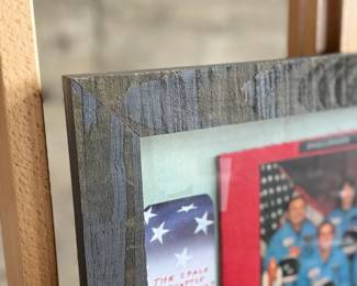 This lot features a curated collection of space memorabilia held and displayed in a wooden frame. Includes an autograph from Christa McAuliffe and much more. This piece measures in frame, 22.5” H x 18.75” W.
