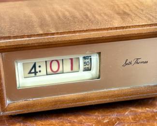 Seth Thomas vintage wooden flip clock featuring a natural woodgrain exterior with a silver-tone faceplate. Displays time using a rotating flip mechanism. Includes an attached electric cord for operation. Minimal signs of wear are visible consistent with age. Tested and in working condition.