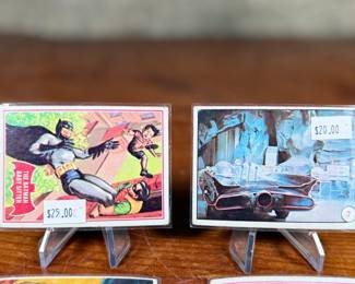 Vintage Batman trading cards, featuring original artwork and comic illustrations. Cards include storylines and engaging captions on the reverse side. Produced by National Periodical Publications, Inc., circa 1960s. Cards are displayed on stands; conditions appear fair with signs of handling and age.