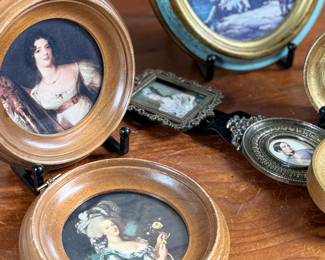 Decorative miniature artworks in various oval and round frames. Frames include painted gold and blue accents, some marked ‘Made in Italy’. Depicting classical European and romantic scenes, including individuals and landscapes. Constructed from materials resembling wood and metal with exposed backing hardware. Intricately set, ideal for wall or tabletop display.