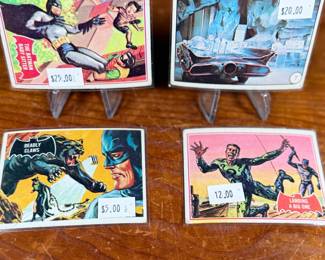Vintage Batman trading cards, featuring original artwork and comic illustrations. Cards include storylines and engaging captions on the reverse side. Produced by National Periodical Publications, Inc., circa 1960s. Cards are displayed on stands; conditions appear fair with signs of handling and age.