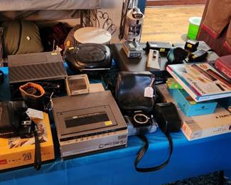 Whole table of cameras  video equipment,  splicing machine, vcr, audio/video equipment,  board games, sleeping bags, signal converter
