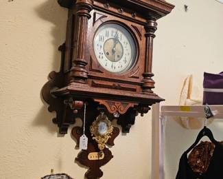 Ornate carved wooden German wall clock with Roman numerals and decorative pendulum. Clock face is uraniun.