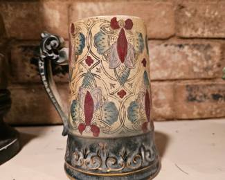 A decorative ceramic mug with ornate handle and floral pattern.