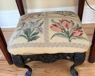 Victorian-style footstool featuring a needlepoint tapestry seat with floral motifs and a black cast iron frame