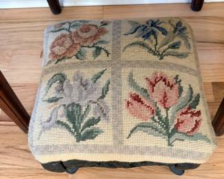 Victorian-style footstool featuring a needlepoint tapestry seat with floral motifs and a black cast iron frame