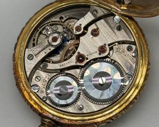 Closeup of interior of the 18K yellow gold Gruen pocket watch, late 19th/early 20th century. The face is adorned with intricate tri-color gold (white, rose, and yellow) floral engravings. The watch is housed in an 18K gold case, featuring heavily chased, ornate scrollwork; inscribed inside with “Swiss” and stylized logo for Dietrich Gruen & Sons, and numerals 125758.