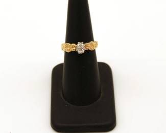 A yellow gold engagement ring featuring an oval-cut diamond in a textured filigree setting