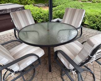 Round glass-topped patio table with 4 armchairs (rocker and swivel) with cushions
