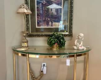 Framed cafe scene ($100.00), vintage brass and glass console table ($350.00), table lamp with urn form base ($25.00), angel figure ($10.00)