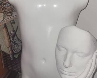 Torso mannequin and plaster sculpture face in hand on black base.