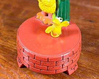 This lot features a 1976 Gorham Sesame Street Big Bird and Little Bird music box. The music box features Big Bird standing next to a “Sesame Street” signpost. It operates using a magnet mechanism that makes the small bird dance on the brick-patterned base. It was produced by the Gift World of Gorham and is in working condition.