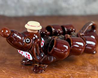 This lot features a vintage dachshund-shaped ceramic decanter set, often referred to as a "drunken dog" liquor flask set. In excellent condition and measures, 5” H x 13” W x 7” D.