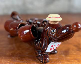 This lot features a vintage dachshund-shaped ceramic decanter set, often referred to as a "drunken dog" liquor flask set. In excellent condition and measures, 5” H x 13” W x 7” D.