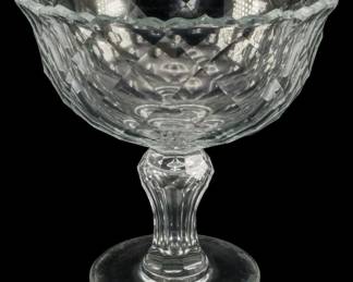 144 - Large Glass Compote 10"x10" (Description): Large glass compote featuring a decorative  bowl with a faceted pattern and scalloped  rim, supported by a fluted pedestal base.  Measures 10 inches by 10 inches.
