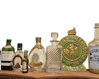 3954 - Collection of Vtg Liquor Bottles & Decanters (Description): Group of liquor bottles including various  vintage decanters, novelty bottles, and  collectible spirits containers. The  collection features an assortment of styles  including a Native American chief figural bottle, cut glass decanters, and bottles with  original labels from various distillers and  wineries. Also includes a decorative 1972  Greater Greensboro Open golf plaque.