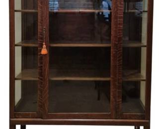 4006 - Original Finish Mission Oak Display Cabinet (Description): An original finish Mission Oak cabinet  featuring classic Arts and Crafts styling.  The cabinet has two glass-paneled doors  flanking a central wood panel, with three  interior shelves for display storage. The piece rests on straight legs with casters for  easy movement and retains its original  hardware with a decorative tassel key.  Measures 59 inches tall by 44 inches wide by  15 inches deep.