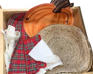 928 - Kitchen Drawer Lot w/ Placemats & Linens (Description): Kitchen drawer lot containing an assortment  of table linens and serving accessories.  Includes woven jute placemats, red plaid  cloth napkins, white lace-trimmed linens, and  a decorative wooden turkey-shaped serving dish or tray in orange with painted details.  Items are presented in a wooden storage box.