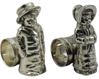 89 - 2 Meriden Britannia Co Silver Plate Napkin Holders (Description): Vintage silver plate figural napkin holders  by Meriden Britannia Co. The pair depicts a  boy and girl in period dress, each figure  holding a napkin ring. Measures 4.5 inches  tall.