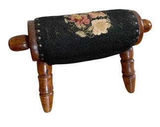 1351 - Vintage Needlepoint Floral Footstool (Description): Vintage needlepoint footstool featuring a  floral design on a black ground. The  cushioned top is secured with decorative  brass tacks and supported by turned wooden  legs with extending wooden handles on each end. Measures 20 1/2" x 11".