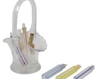 891 - Glass Basket w/ Assorted Vtg Glass Vials (Description): A decorative glass basket containing an  assortment of vintage glass vials. The basket  measures 5.5 inches in height and features a  curved handle. The collection includes  various colored glass vials with stoppers, showcasing different striped patterns in hues  of blue, yellow, and red.
